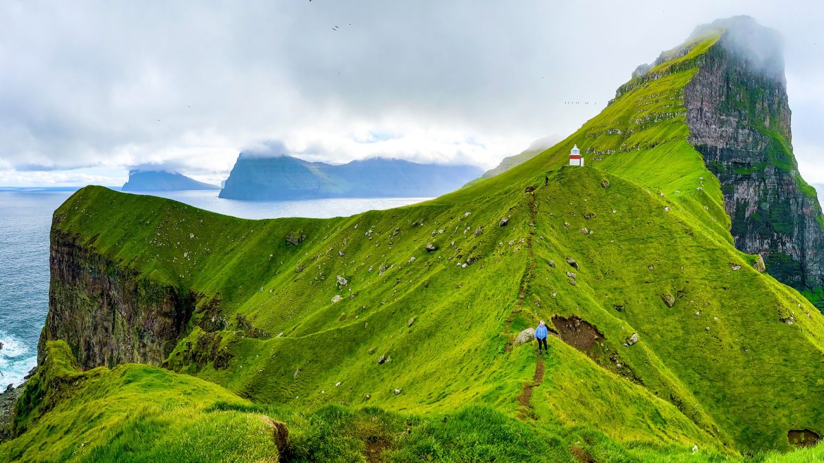 Osoba chodząca po szlaku trekkingowym na tle gór i kapliczki.