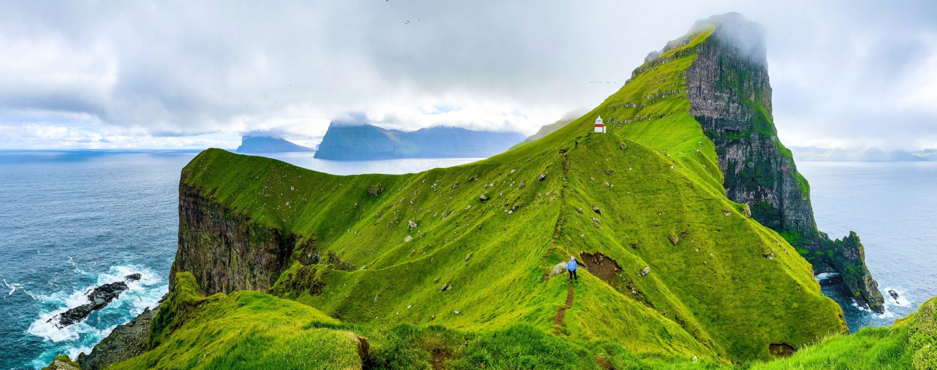 Osoba chodząca po szlaku trekkingowym na tle gór i kapliczki.